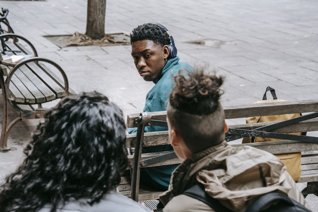 Back view of anonymous classmates sitting behind black friend and gossiping on schoolyard